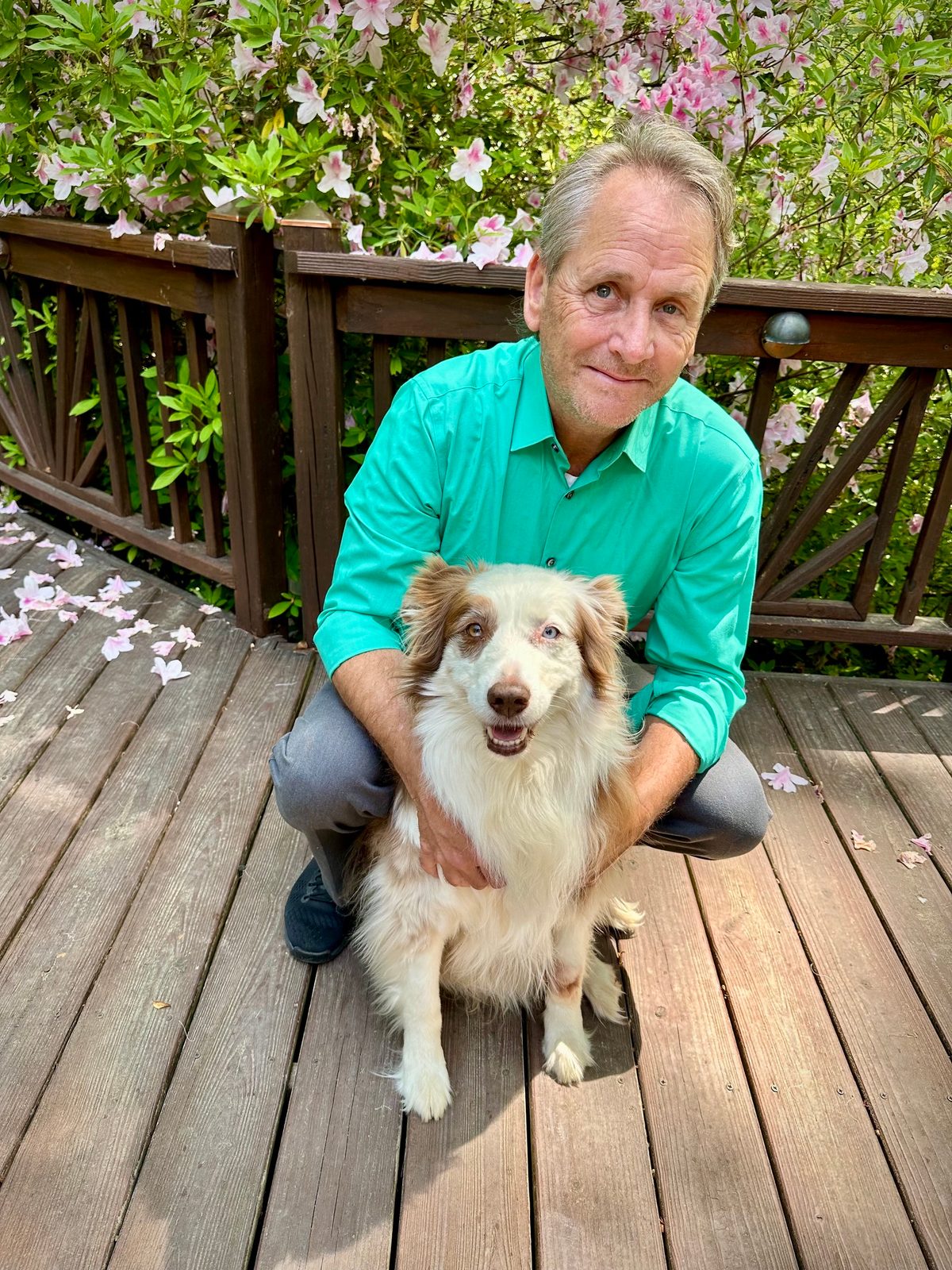 Brian crouching on a wooden deck with his Australian Shepherd